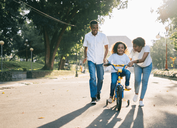 mother and father teaching their daughter how to ride a tricycle